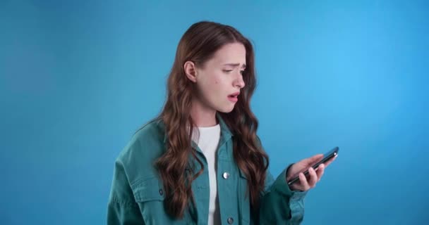 带着手机的令人失望的年轻女人得到了坏消息 浅蓝色背景 图库视频