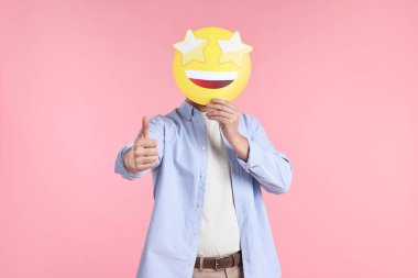 Gözler yerine yıldızlı ifade tutan ve pembe arka planda baş parmağını gösteren bir adam.