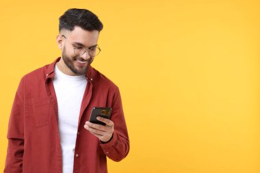Mutlu genç adam sarı arka planda akıllı telefon kullanıyor, mesaj için boşluk