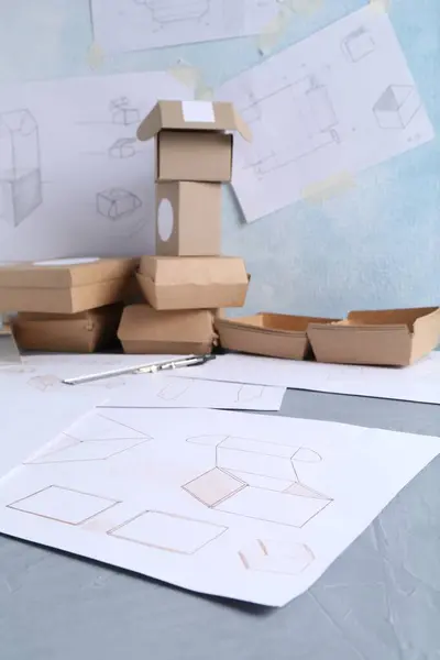 Creating packaging design. Drawings and boxes on blue textured table, closeup