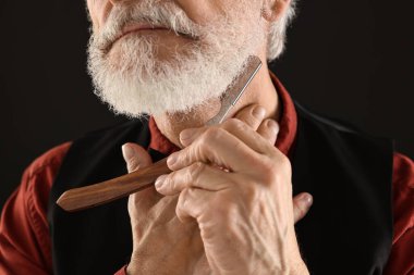 Siyah arka planda jiletle tıraş olan adam, yakın plan.