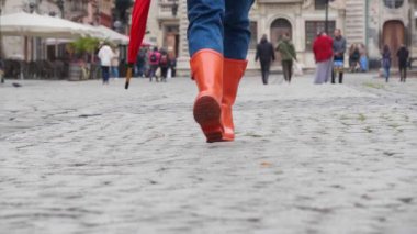 Parlak turuncu çizmeli kadın şehirde kameraya doğru yürüyor.