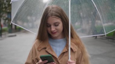 Dışarıda birini beklerken şemsiyeli güzel bir kadın cep telefonu kullanıyor.
