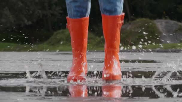 Frau Leuchtend Orangefarbenen Regenstiefeln Springt Freien Eine Pfütze Nahaufnahme — Stockvideo