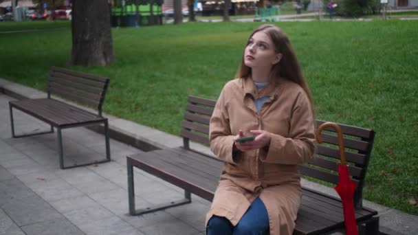 Fiatal Gyönyörű Padon Használja Mobiltelefon Szabadban Majd Kinyitja Esernyő Elsétál — Stock videók