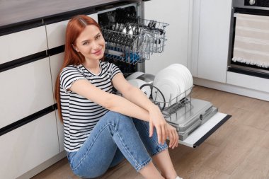 Mutfakta açık bulaşık makinesinin yanında oturan güzel kadın.