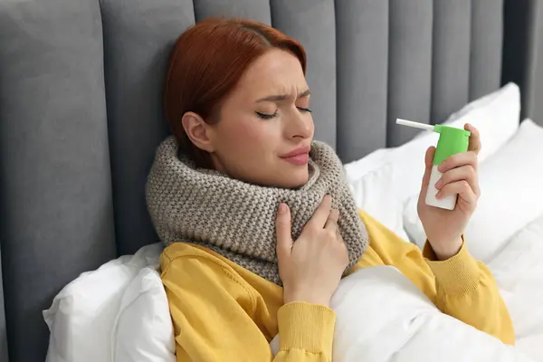 Young woman with scarf holding throat spray in bed