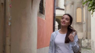 Sırt çantalı mutlu genç bir kadın şehir sokaklarında yürüyor.