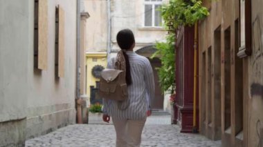 Sırt çantalı genç bir kadın şehir sokaklarında yürüyor.