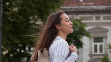Sırt çantalı mutlu genç bir kadın şehir sokaklarında yürüyor.