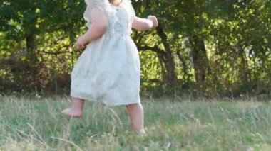 Yeşil çimenlerde yalınayak yürüyen tatlı küçük kız. Kamera çocuğu takip ediyor
