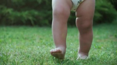 Küçük bebek yeşil çimenlerde yalınayak yürüyor, yakın plan.