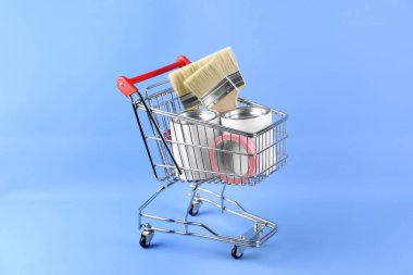 Açık mavi arka planda boyama araçları olan küçük bir alışveriş arabası.