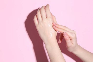 Kadın pembe arka plana krem sürüyor, yakın plan.