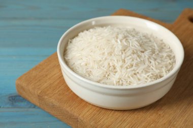 Tabakta çiğ basmati pilavı, açık mavi ahşap masa, yakın plan.