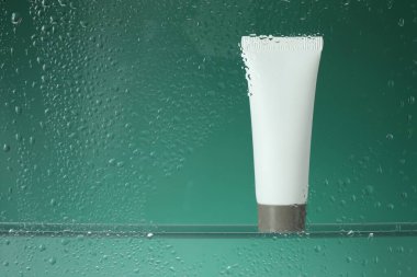 Yeşil arka planda nemlendirici krem bulunan bir tüp. Islak camdan görülüyor. Metin için boşluk