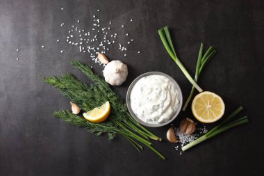 Dereotlu lezzetli yoğurt, yeşil soğan, limon ve sarımsak siyah arka planda, düz konum