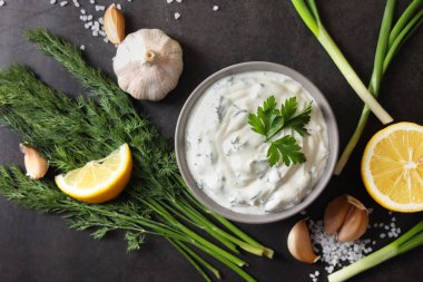 Dereotlu lezzetli yoğurt, yeşil soğan, limon ve sarımsak siyah arka planda, düz konum
