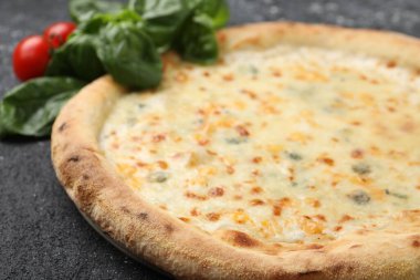 Lezzetli peynirli pizza, fesleğen ve domates siyah desenli masa, yakın plan.