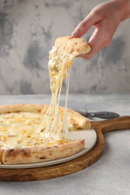 Açık gri masada lezzetli peynirli pizza yiyen bir kadın, yakın plan.