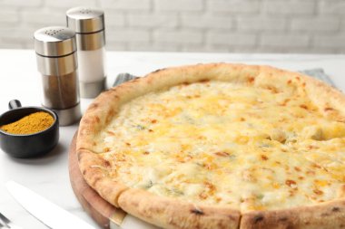 Lezzetli peynirli pizza ve baharatlar beyaz masada, yakın plan.