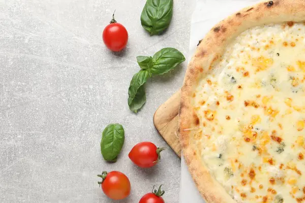 Lezzetli peynirli pizza, fesleğen ve domatesler açık gri masada, düz yayılmış. Metin için boşluk