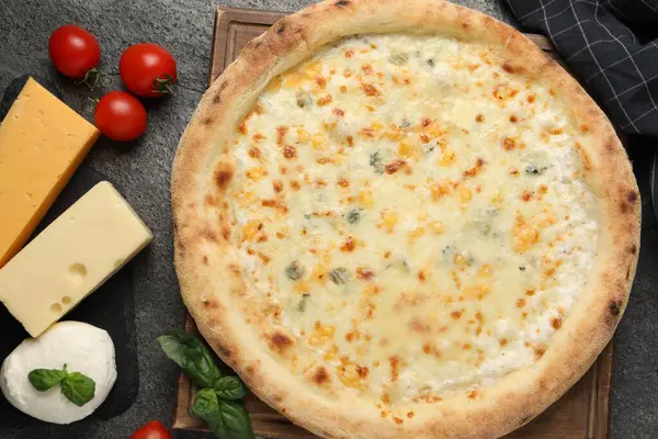 Lezzetli peynirli pizza ve malzemeler koyu gri masada, düz yatıyordu.