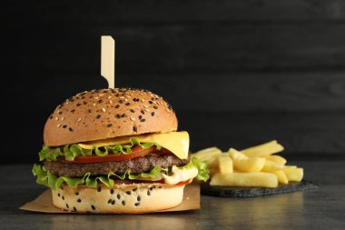 Lezzetli köfteli burger ve gri masada patates kızartması, koyu arka planda, mesaj için yer var.