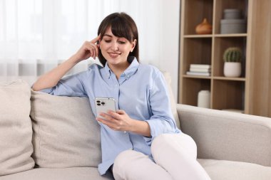 Evdeki kanepede akıllı telefon kullanan güzel bir ev hanımı.