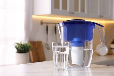 Mutfaktaki beyaz mermer masada su filtresi sürahi ve cam var, yakın plan. Metin için boşluk