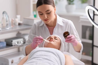 Kozmetik uzmanı klinikte kadının yüzüne maske takıyor.