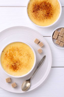 Lezzetli creme brulee kaseler, şeker küpleri ve kaşık beyaz ahşap masa, düz yatıyordu