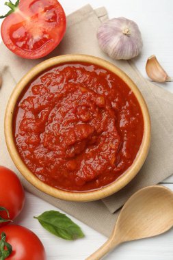 Ev yapımı domates sosu kasede, kaşıkta ve taze malzemeler beyaz ahşap masada, düz yerde.