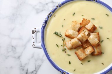 Lezzetli patates çorbası, kıtır ekmek ve biberiye, beyaz mermer masa üzerinde seramik kap, üst manzara. Metin için boşluk