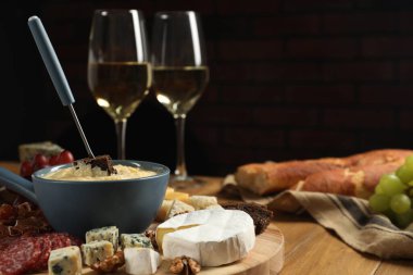 Lezzetli eritilmiş peynirli fondü tenceresi, çatal, farklı atıştırmalıklar ve ahşap masada şarap.