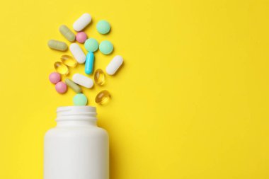 Farklı vitamin hapları ve sarı arka planda bir şişe. Metin için boşluk