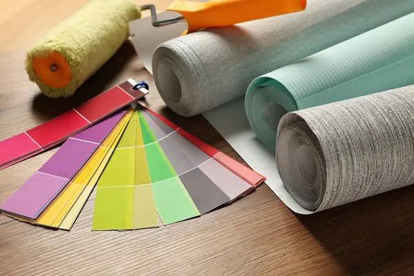 Different wallpaper rolls, roller and color palette samples on wooden table