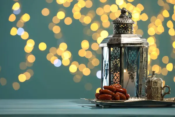 Stock image Traditional Arabic lantern, dates and vintage cup holder on table against dark turquoise background with blurred lights. Space for text