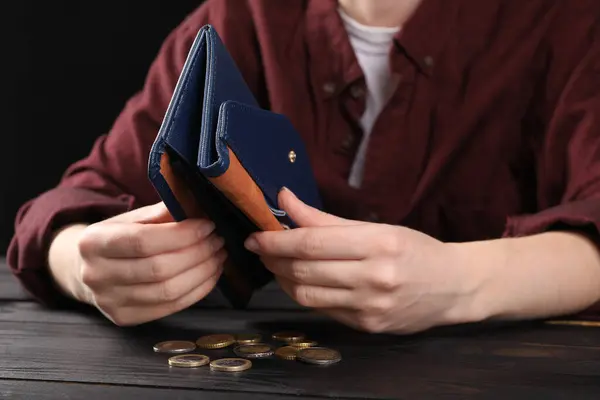 Poverty. Woman with empty wallet and coins at wooden table, closeup