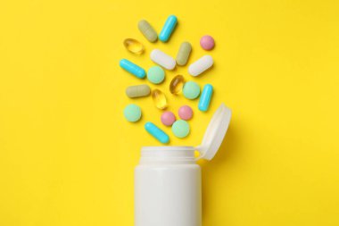 Farklı vitamin hapları ve sarı arka planda bir şişe..