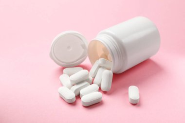 Pembe arka planda şişe ve vitamin kapsülleri