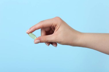 Açık mavi arka planda vitamin kapsülü tutan kadın, yakın plan. Sağlık takviyesi