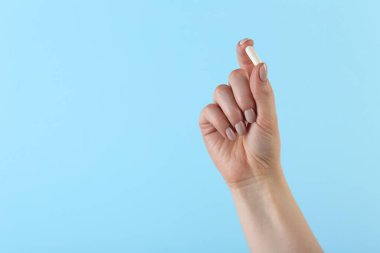 Açık mavi arka planda vitamin kapsülü tutan kadın, metin için yeri olan yakın plan. Sağlık takviyesi