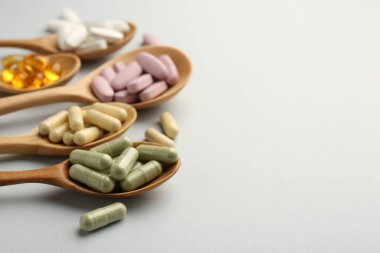 Açık gri arka planda kaşıklardaki farklı vitamin hapları, mesaj için yer açılacak şekilde yakın plan. Sağlık takviyesi