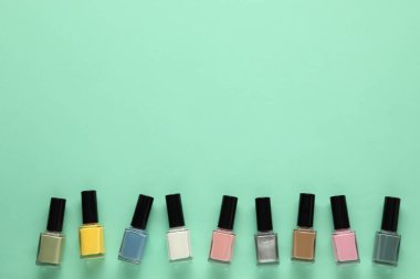 Turkuaz arka planda, parlak tırnak cilasını şişelere koyup düz bir zemine yatırın. Metin için boşluk