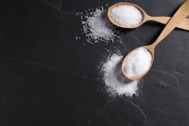 Doğal tuz ve tahta kaşıklar siyah masada, düz yerde. Metin için boşluk