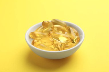 Vitamin kapsülleri sarı arka planda kasede