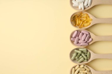 Farklı vitamin hapları soluk sarı arka planda kaşıklarda, düz yerde. Metin için boşluk