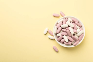 Soluk sarı arka planda, kasede farklı vitamin hapları var. Metin için boşluk
