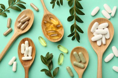 Farklı vitamin kapsülleri kaşık ve turkuaz arka planda yapraklar, düz yatış
